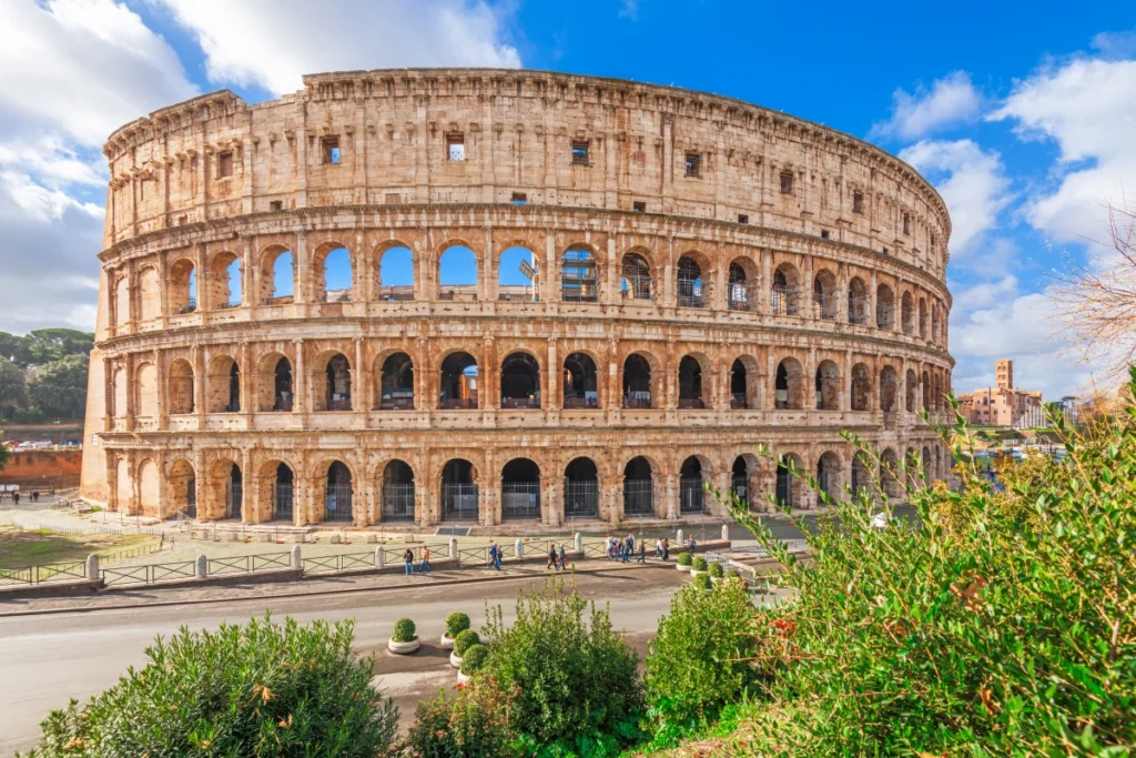 Colisée antique de Rome sous ciel partiellement nuageux avec piétons et végétation au premier plan