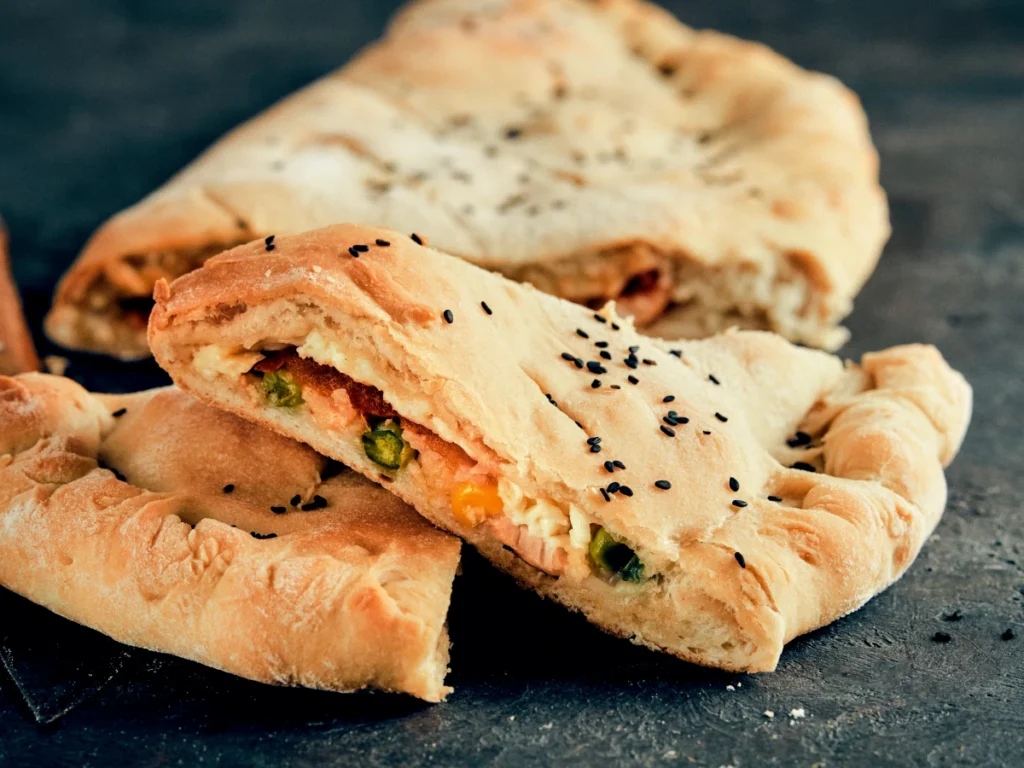 Calzone napolitain coupé, pâte dorée garnie de légumes, fromage et graines noires, recette des maîtres pizzaiolos napolitains